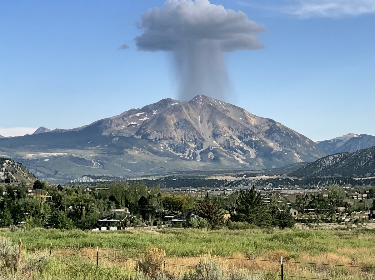 A snow-streaked alpine mountain peak in summer with the storm cell seated directly upon its summit