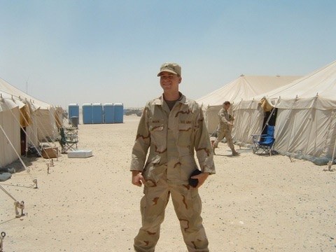 A soldier in desert camouflage standing between rows of tents on sand
