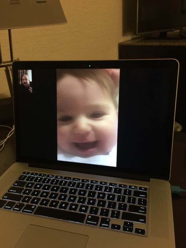 A laptop in a hotel room showing a video call with a smiling baby