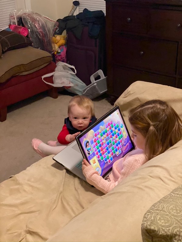 Two small children on a couch, one playing a game on a tablet