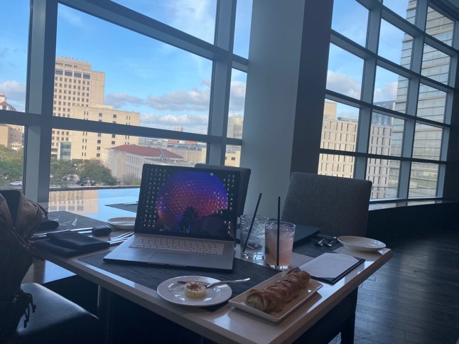 A laptop on a restaurant table beside floor-to-ceiling windows overlooking a city